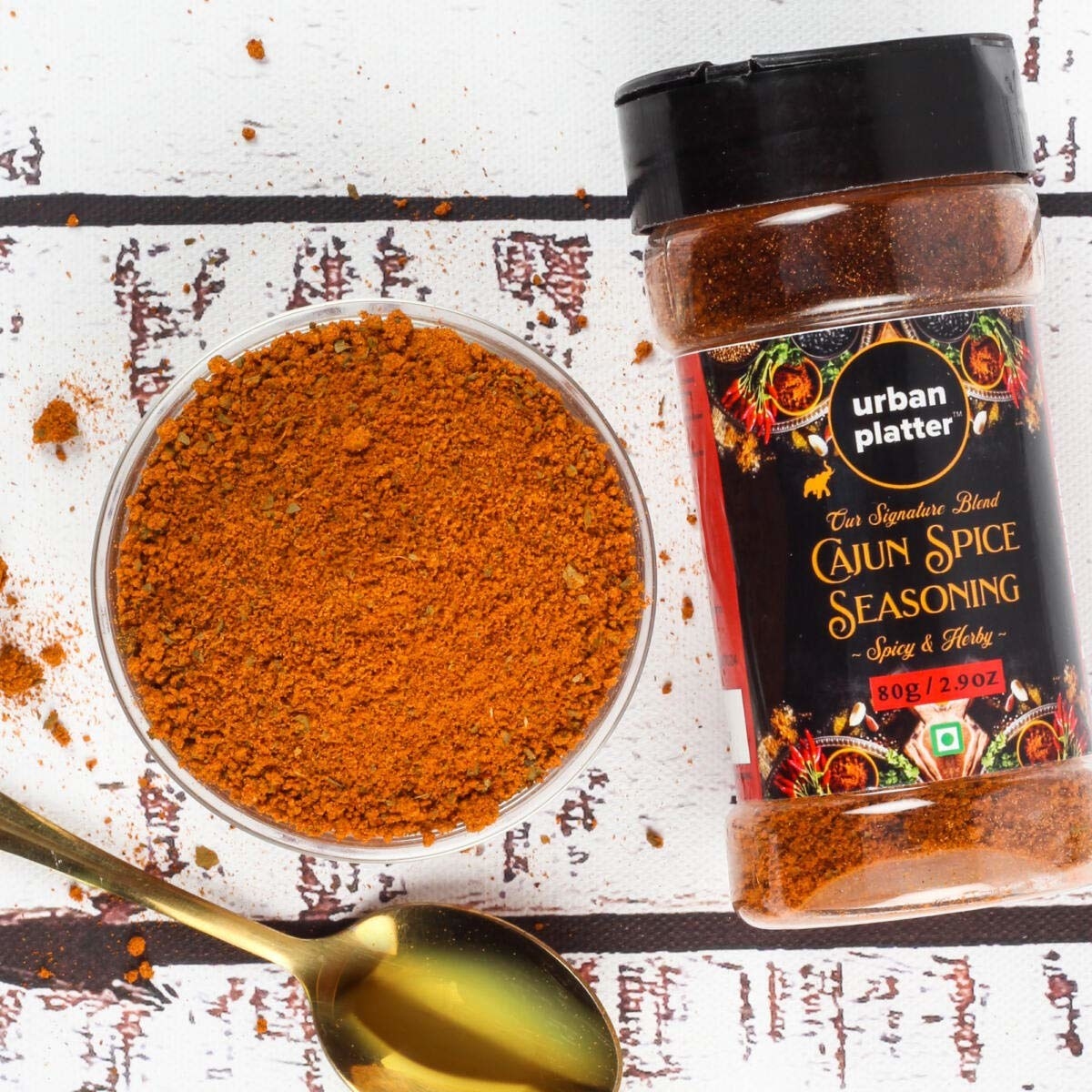 Packaging of the cajun spice seasoning next to the seasoning in a bowl and a spoon