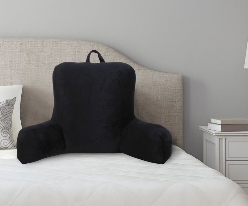 a black backrest pillow with a handle at the top resting on a bed