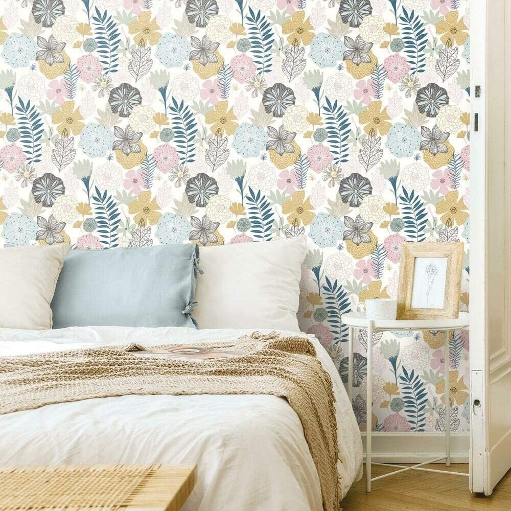 A cozy bed in front of floral wallpaper 