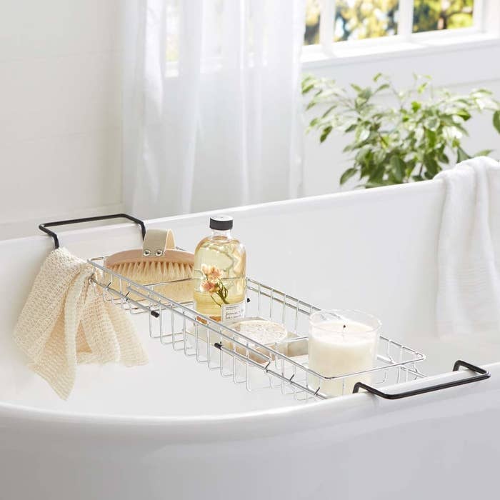 The bathtub caddy pictured on a bathtub with candles and other accessories on it. 