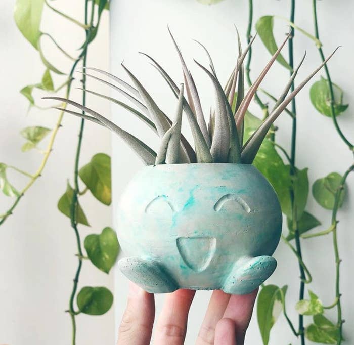 A person&#x27;s hand holding a small plant pot in the shape of a Pokemon Oddish