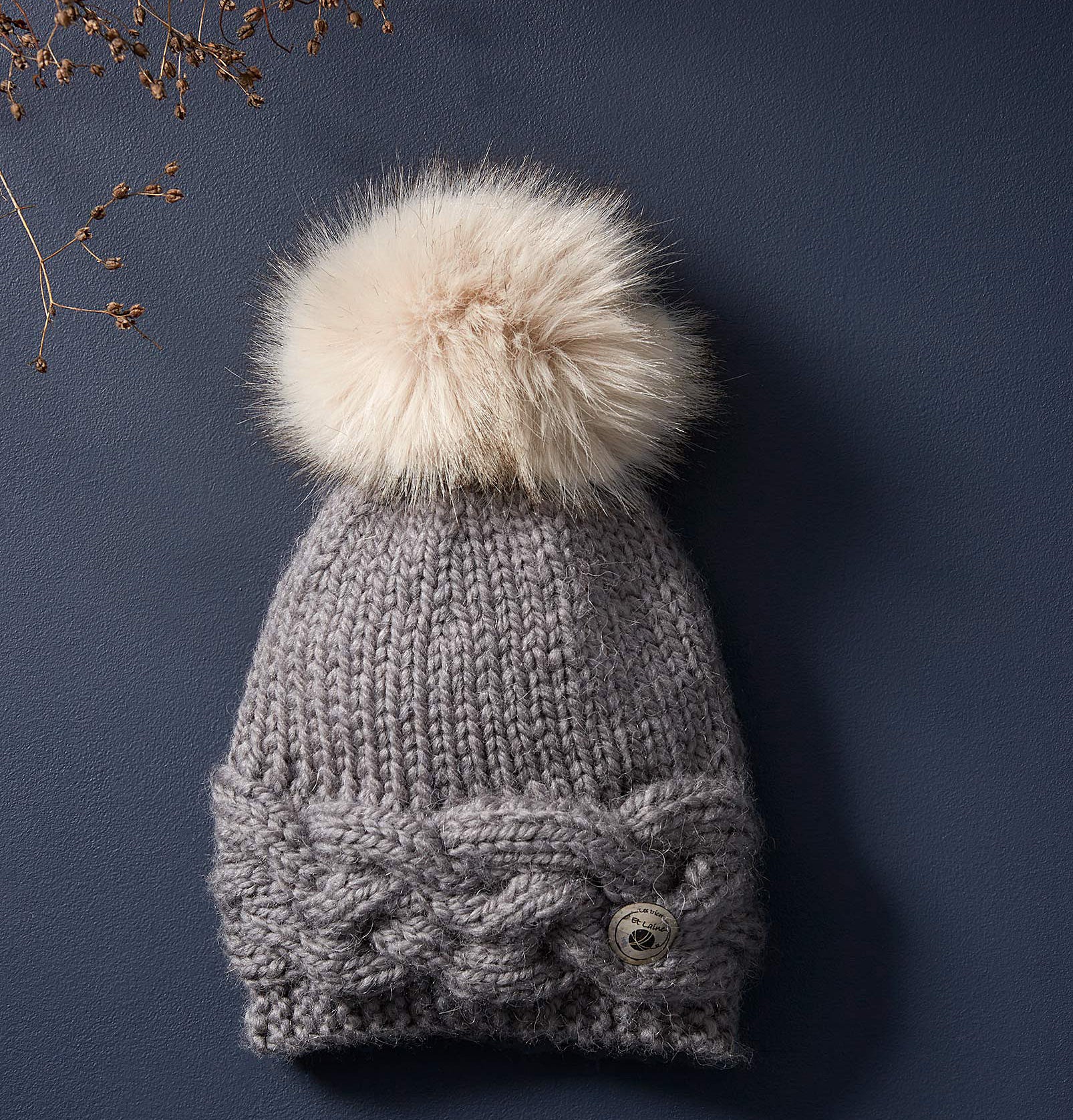 A knit hat with a pom pom on top lying on a plain background