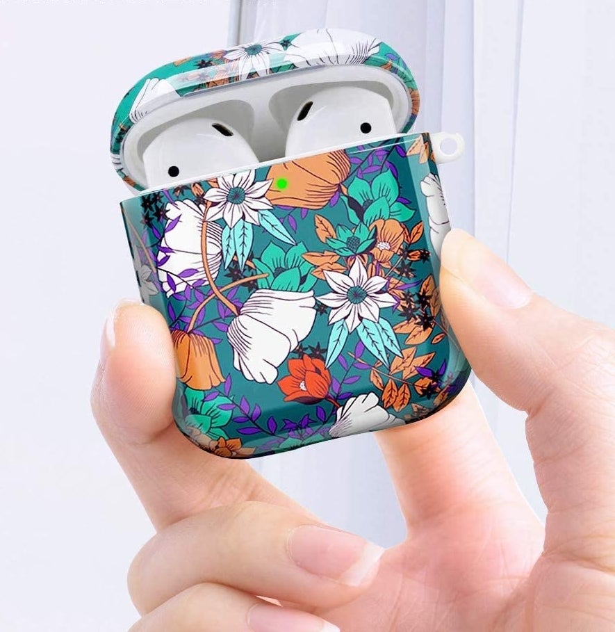 A person holding up a pair of AirPods that are covered in a floral-print case