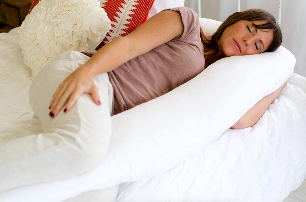 A long u-shaped pillow with a person sleeping on their side in between it 