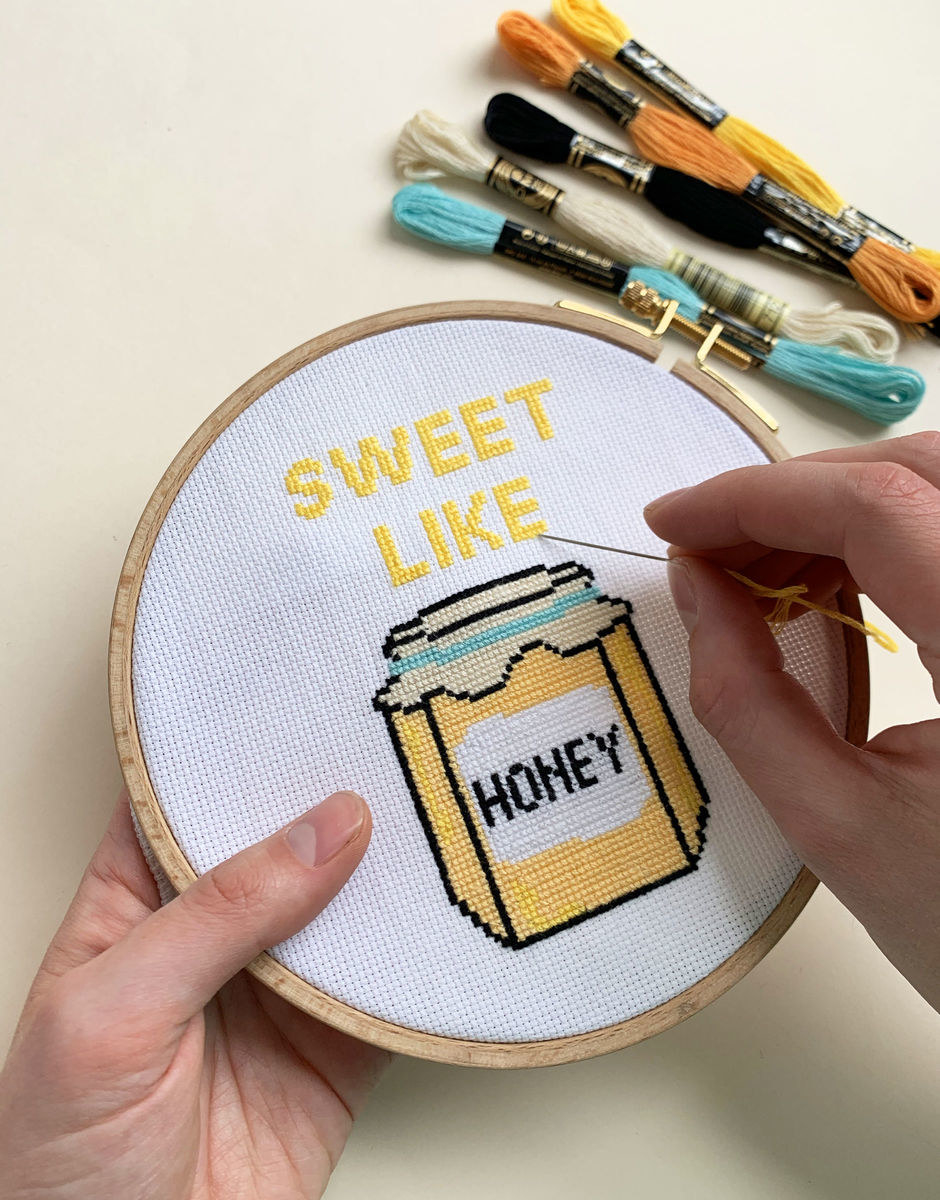 Hands hold colorful cross stitch circle that says &quot;Sweet Like Honey&quot;  with a jar of honey design