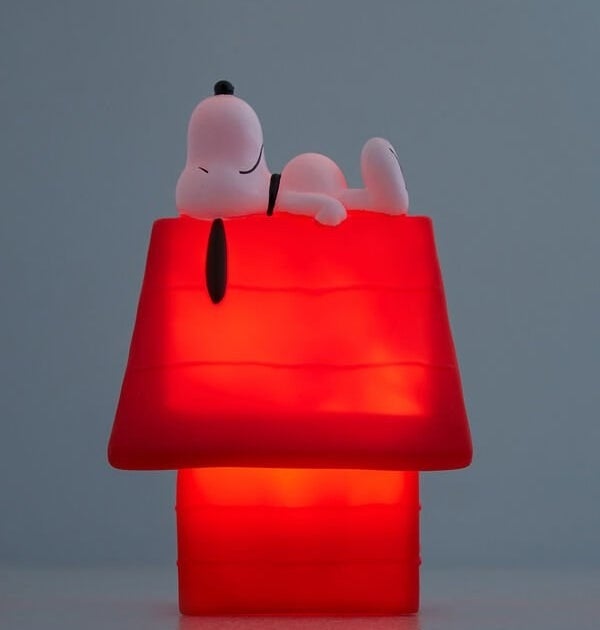 A night light in the shape of a small dog house with a small Snoopy dog lying on top