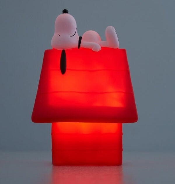 A night light in the shape of a small dog house with a small Snoopy dog lying on top