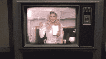 Kesha playing a televangelist and waving from inside a TV