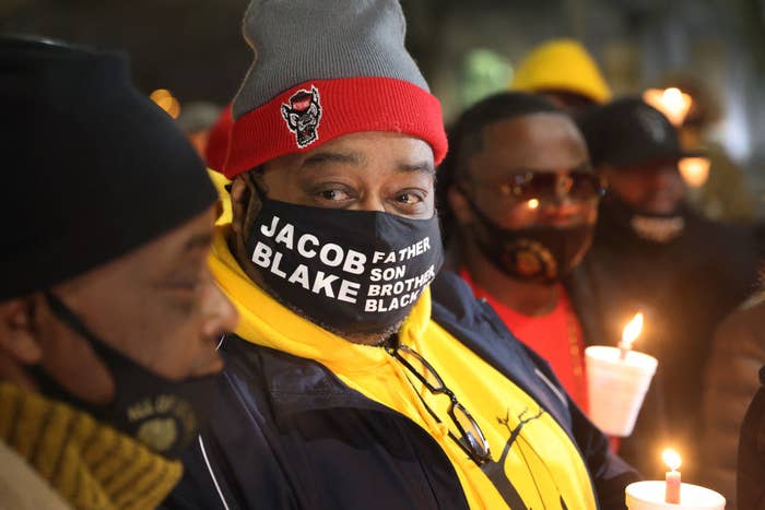 Jacob Blake&#x27;s father holds a candle and wears a face mask that reads &quot;Jacob Blake, father, son, brother, black&quot;