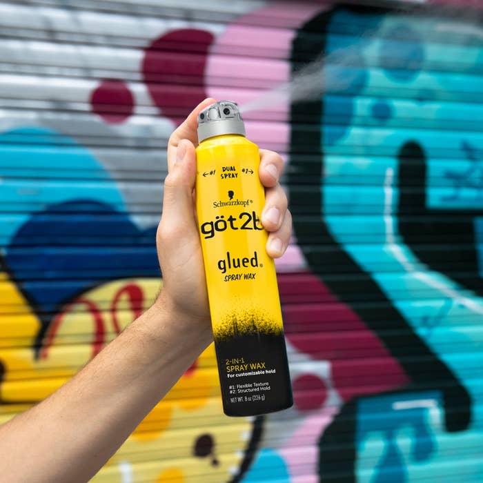 göt2b's Spray Wax held in front of a graffiti-covered wall