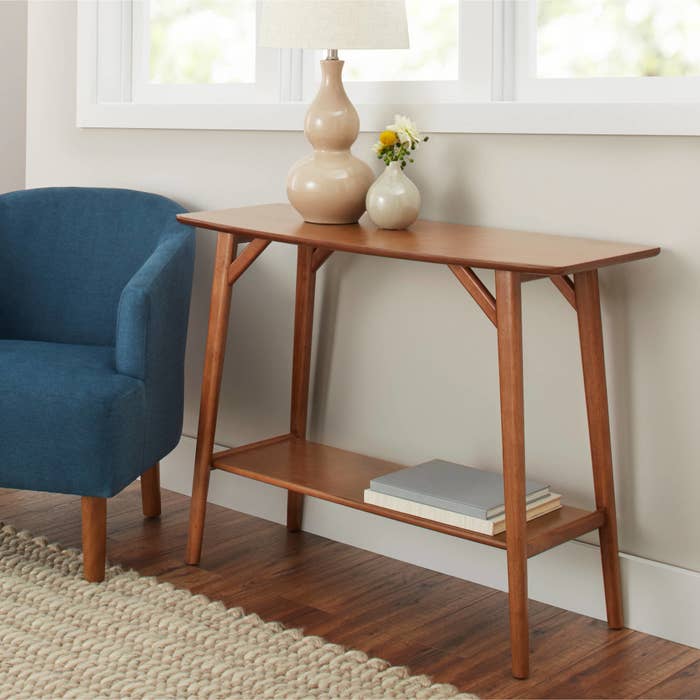 The table, which has long, thin, rounded legs, an open storage shelf near the bottom, and a rectangular top