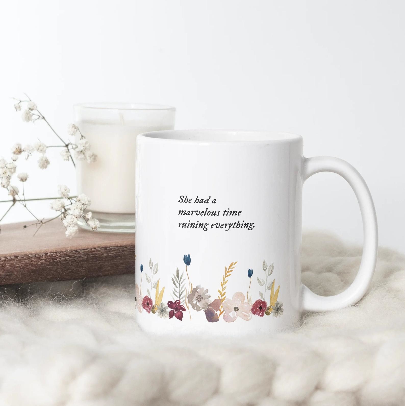 A white mug with watercolor flowers on the bottom that says &quot;she had a marvelous time ruining everything&quot; 