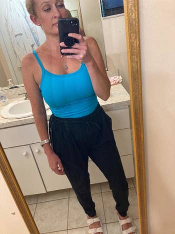 Reviewer wears black tie-waist joggers with a blue cami top and white slide-on sandals