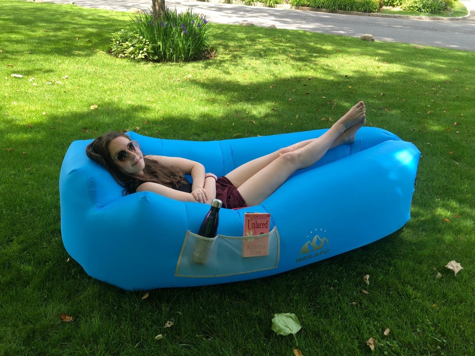 Reviewer lays down in blue inflatable lounger in their backyard