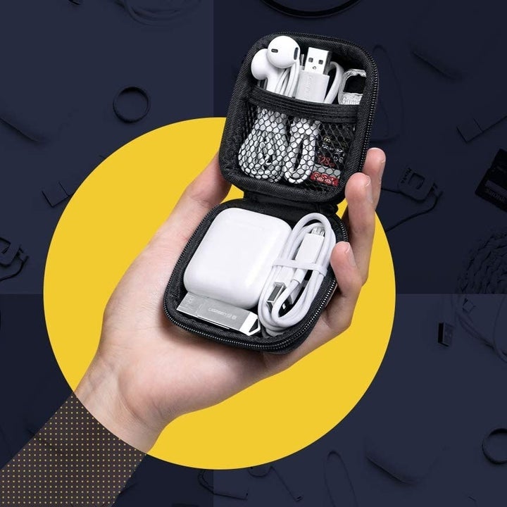 Model holding opened zipper case with AirPods and various accessories