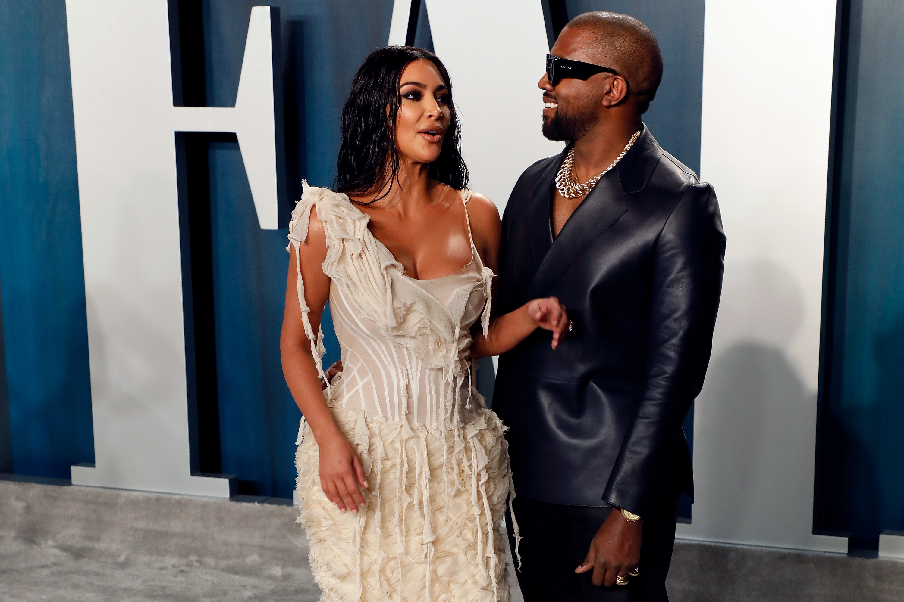 Kim Kardashian and Kanye West wear fashionable outfits in front of a Vanity Fair sign