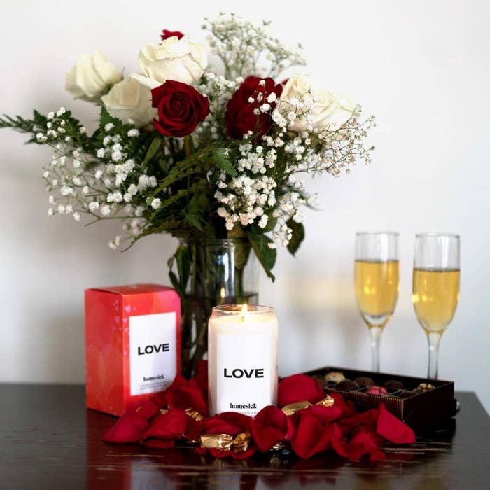 love candle next to box, vase of roses, and two champagne flutes
