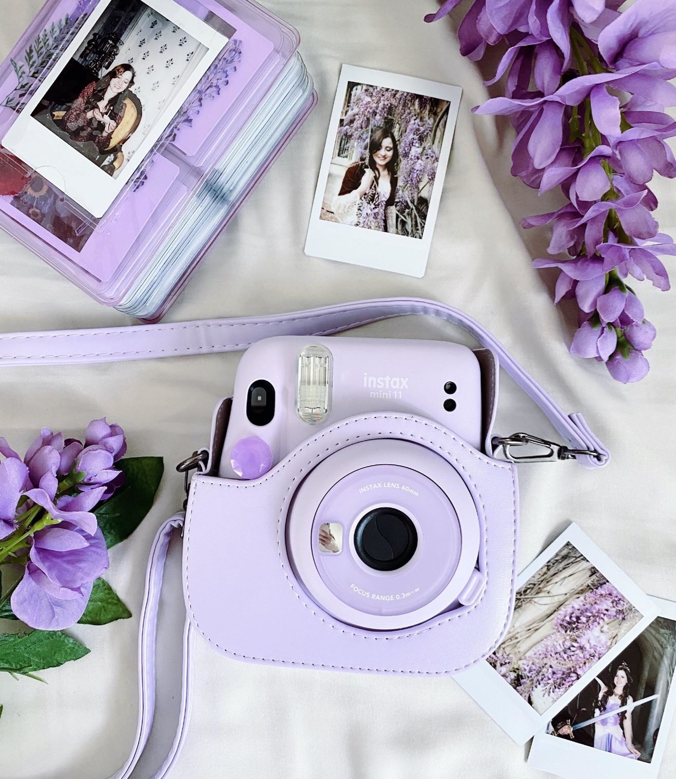 lavender instax camera inside a case laid next to photo prints and flowers