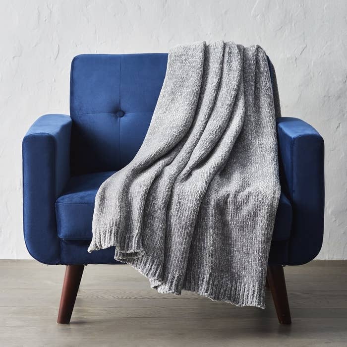 a grey plush throw blanket hanging on a blue chair