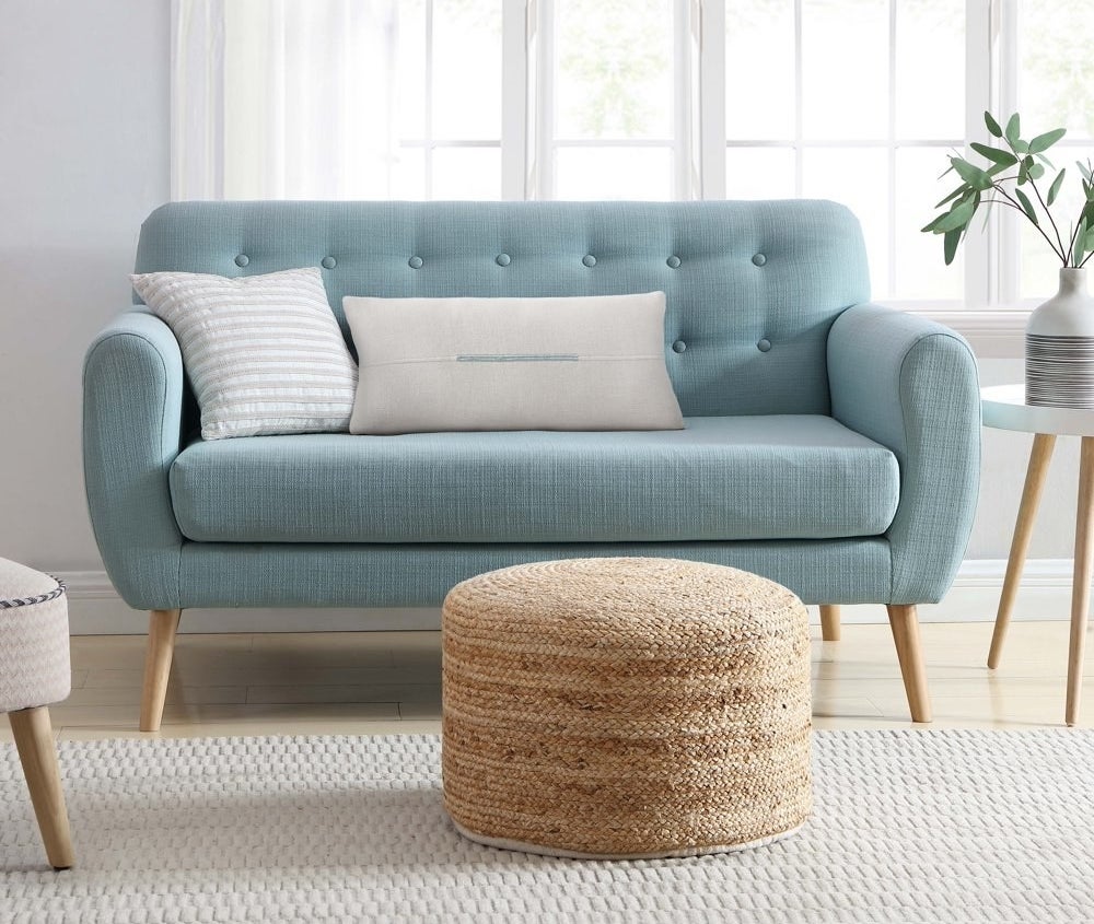 a woven bamboo pouf sitting at the base of a couch
