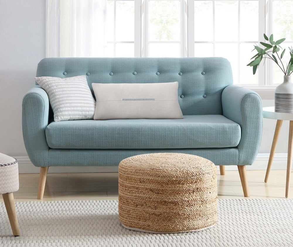 a woven bamboo pouf sitting at the base of a couch