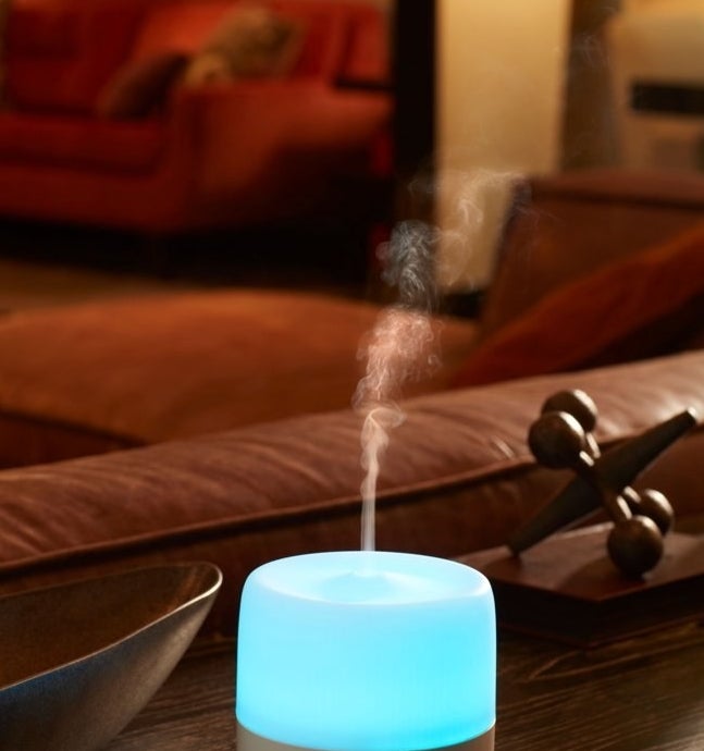 a white, lit diffuser diffusing essential oil mist in the air, sitting on a table