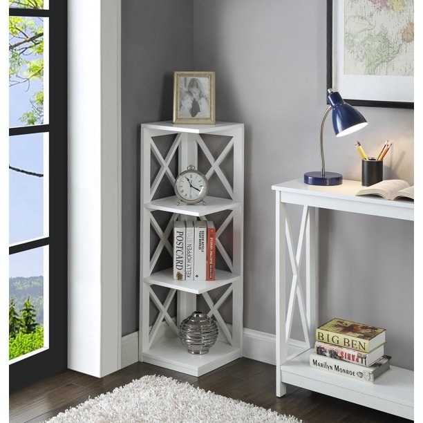 The bookshelf in white, with four shelves for items, and two walls with open weave "X"-shaped supports