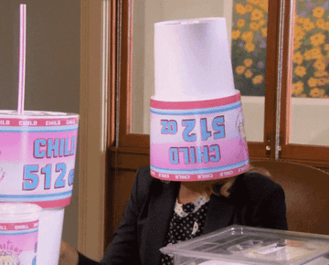 Leslie Knope wearing a giant fast food cup on her head and face-palming