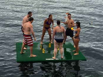Six adults playing with the net and ball game on a floating board in a lake 