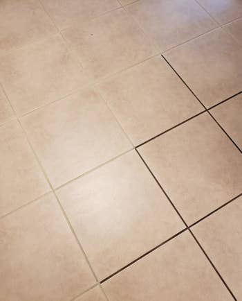 Reviewer's photo which shows half their tiled floor with dirty grout and half with fresh white grout after using the pen