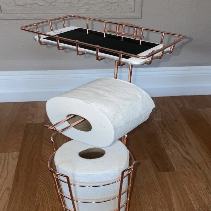 reviewer photo showing the toilet paper stand with their phone on top in the holder