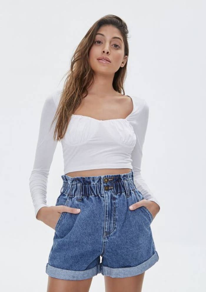 Model is wearing a white top and denim paper bag high waisted shorts