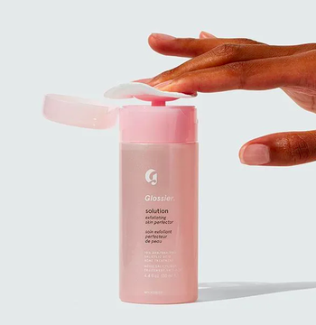 A person pressing a cotton pad into the bottle of Glossier Solution