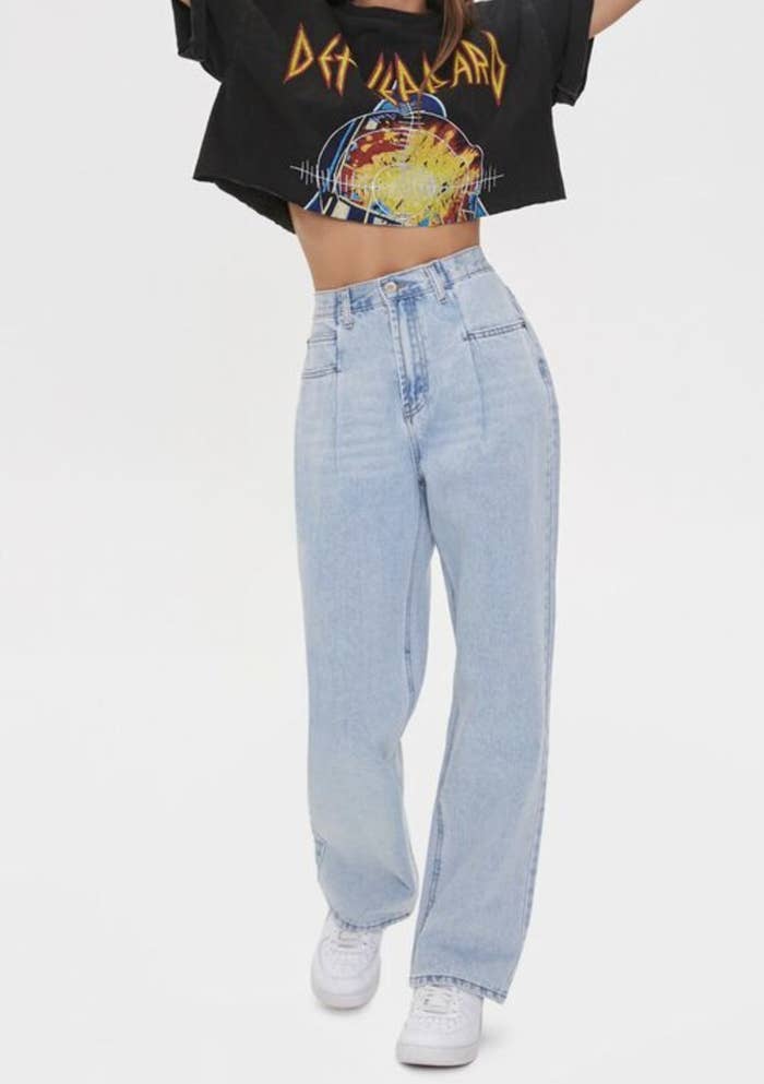 Model is wearing light denim mom jeans, white sneakers, and a graphic tee