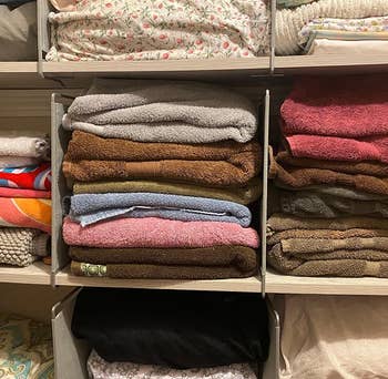 Reviewer photo showing shelf dividers used to separate stacks of towels in their linen closet