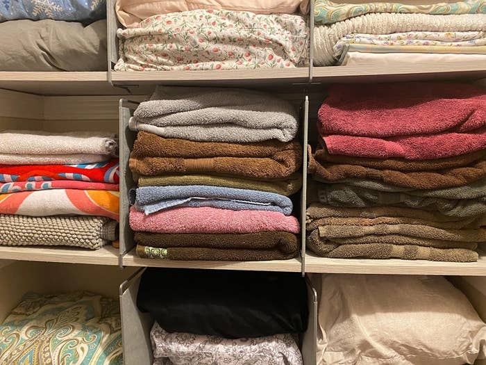 reviewer photo showing shelf dividers used to separate stacks of towels in their linen closet 