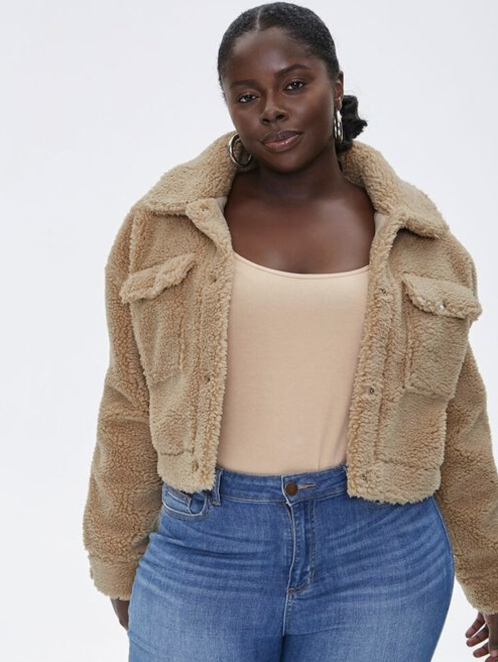 Model is wearing a tan sherpa jacket, beige tank top and blue jeans