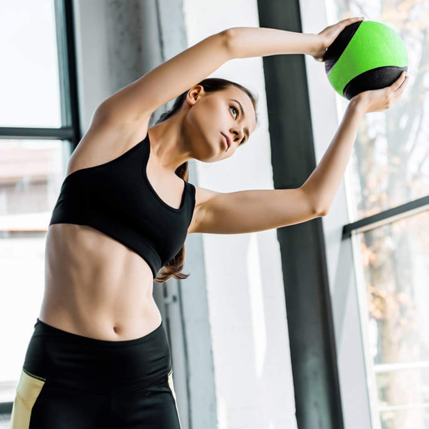 A person doing a side bend while holding a medicine ball over their head 