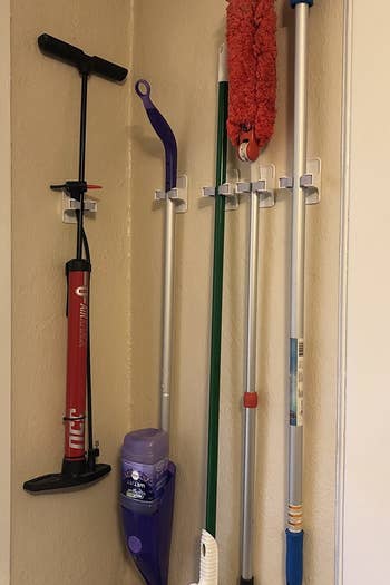 reviewer photo showing the individual clips arranged on a wall to hold a brom, Swiffer, duster and tire pump 
