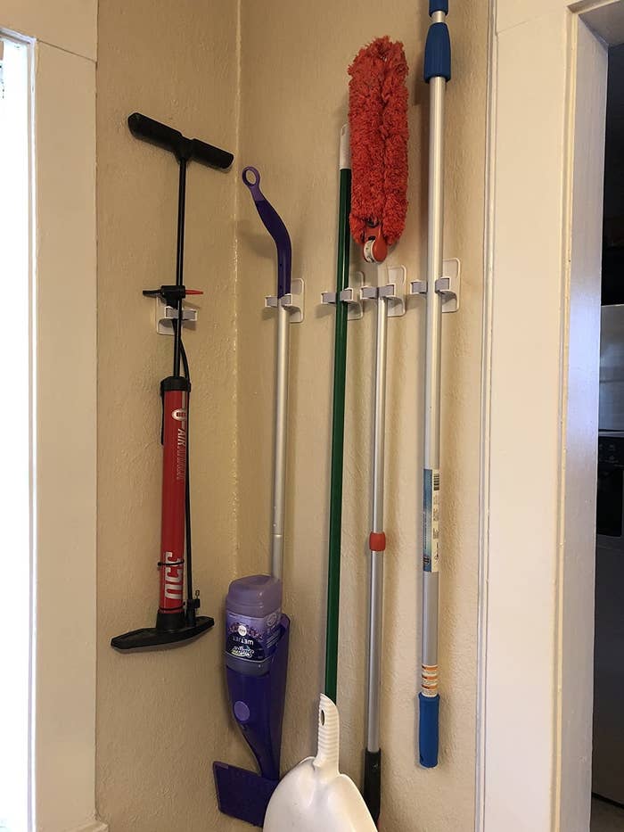 reviewer photo showing the individual clips arranged on a wall to hold a brom, Swiffer, duster and tire pump 