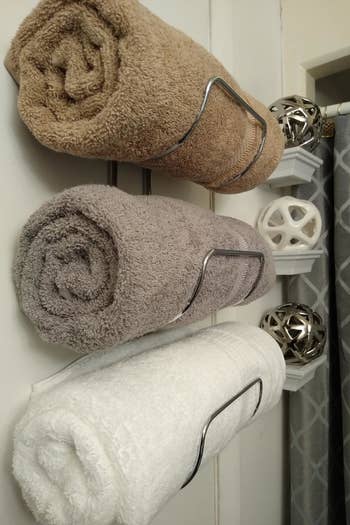 reviewer photo showing side view of towel holder with 3 towels rolled in them 