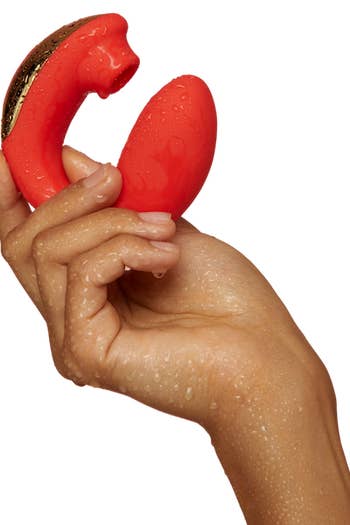 A hand holding the small curved red and gold toy with a suction head and insertable end