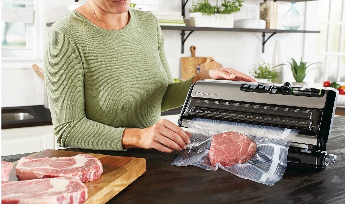 person using a vacuum sealer to suck the air out of a plastic bag with meat in it