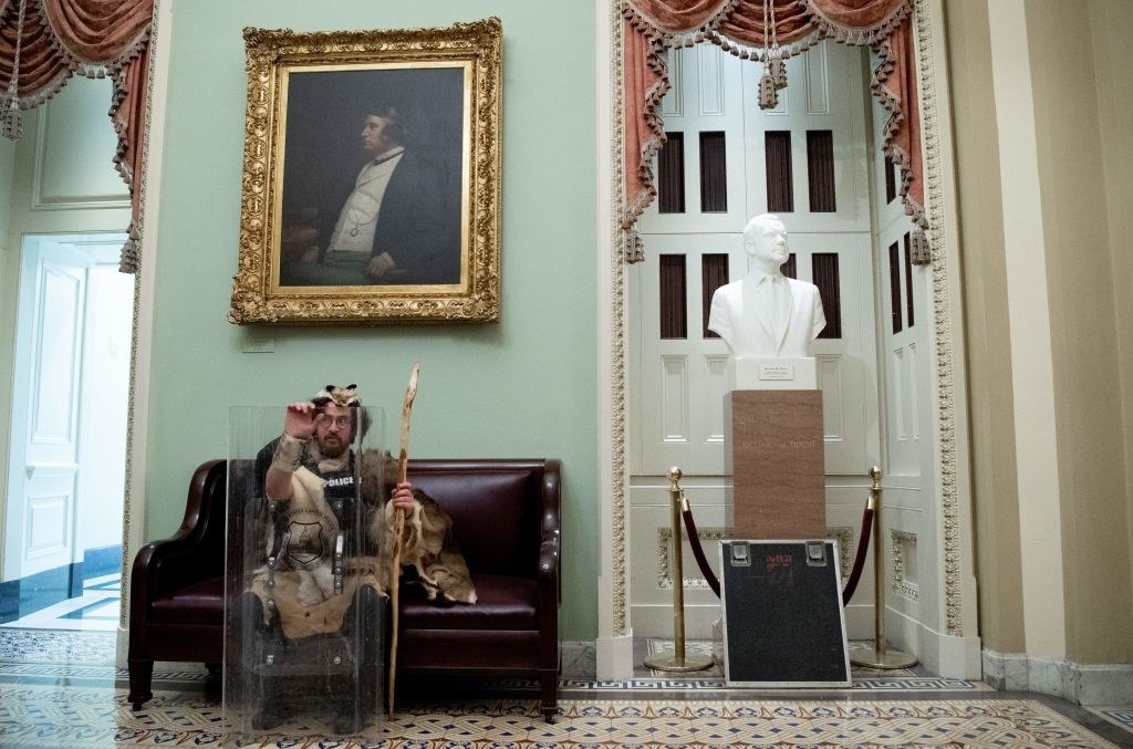 Rioter casually sitting on a couch next to a bust inside the Capitol after storming the building