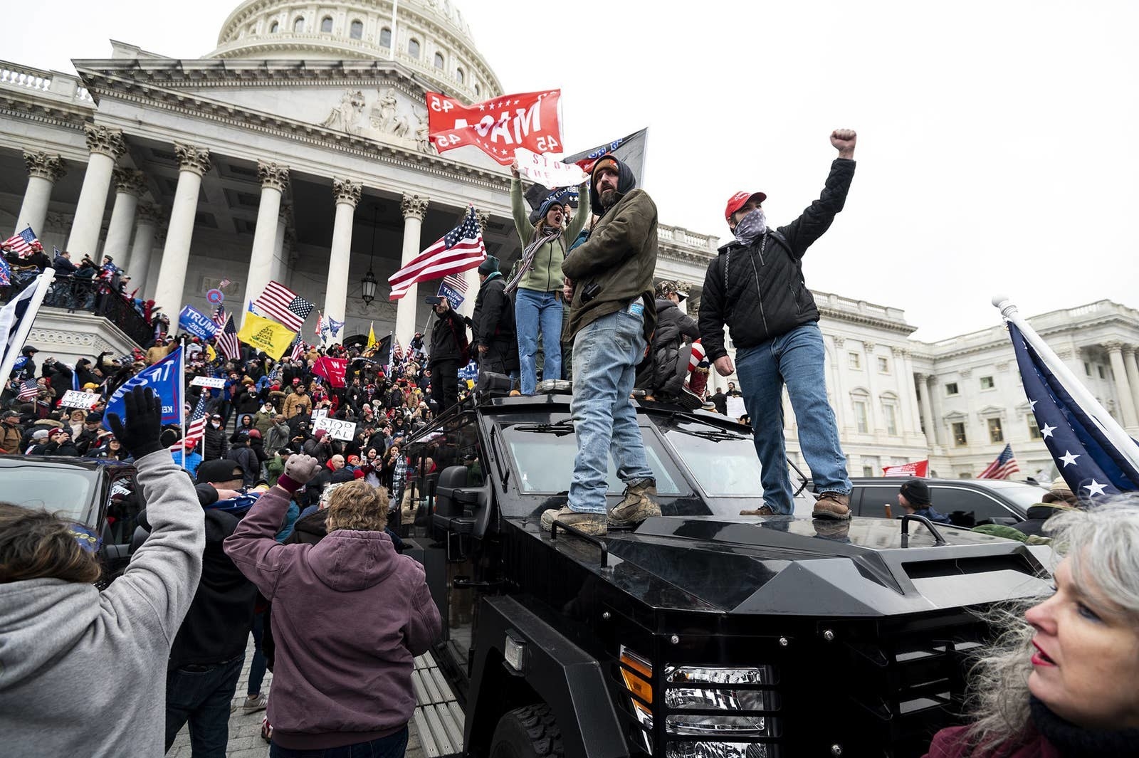 Trump-supporting rioters storming the Capitol building in, with two men standing on the hood of an armored car and others waving flags