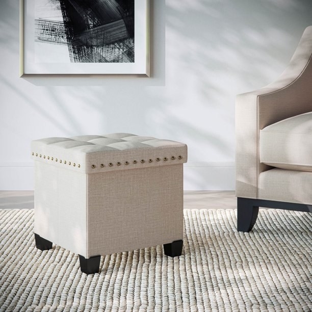 The ottoman, which is cube-shaped, and has tufting on top and nailhead trim around the top sodes