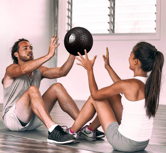 Two people sitting on the floor throwing a medicine ball to each other 