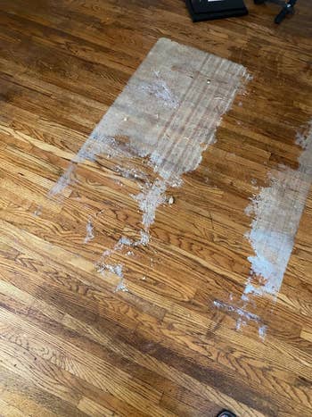 A reviewer's photo of their first attempt to removed sticky residue from their hardwood floor using the formula