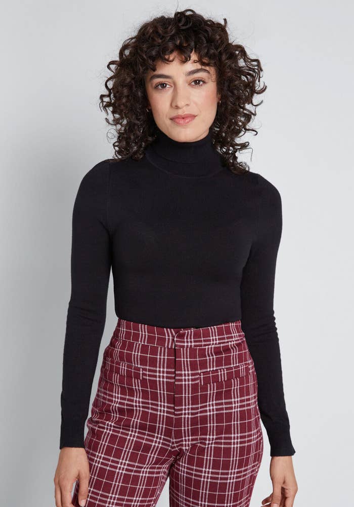 Model wears the black turtleneck with red and white checked pants