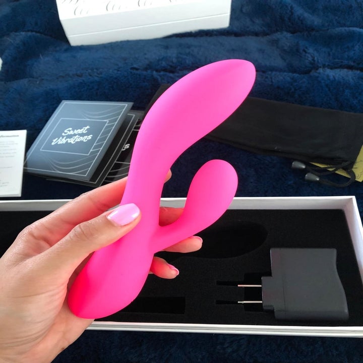 Reviewer photo of their hand holding the pink rabbit-style vibe above the box with the charger